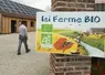 Agriculteur marchant dans sa cour de ferme avec au premier plan une pancarte indiquant "Ici ferme bio"
