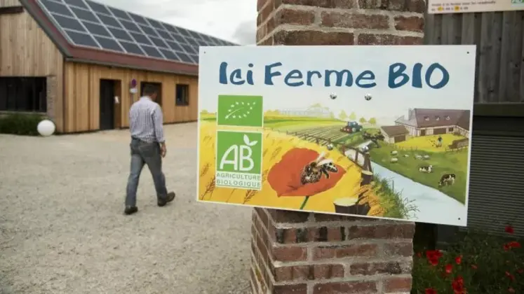 Agriculteur marchant dans sa cour de ferme avec au premier plan une pancarte indiquant "Ici ferme bio"