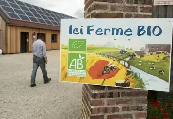Agriculteur marchant dans sa cour de ferme avec au premier plan une pancarte indiquant "Ici ferme bio"