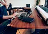 Un Millennial boit une boisson à la paille dans un gobelet jetable tout en travaillant sur son ordinateur portable, son smartphone posé à côté.