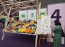 stand à l'entrée d'un salon fruits et légumes. Etal de fruits et légumes, plan du salon et une visiteuse qui le consulte