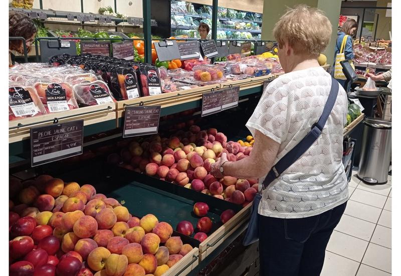 Un rayon de fruits d'été dans un supermarché. Une cliente choisit des pêches.