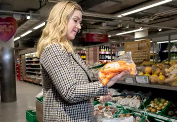 Cliente regardant un pack de carottes dans un magasin Waitrose.