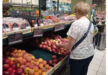 Un rayon de fruits d'été dans un supermarché. Une cliente choisit des pêches.