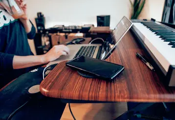 Un Millennial boit une boisson à la paille dans un gobelet jetable tout en travaillant sur son ordinateur portable, son smartphone posé à côté.