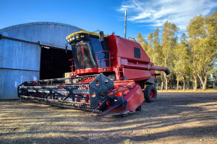 Red harvesting machine with no visible mark parked in front of a shed in a rural establishment