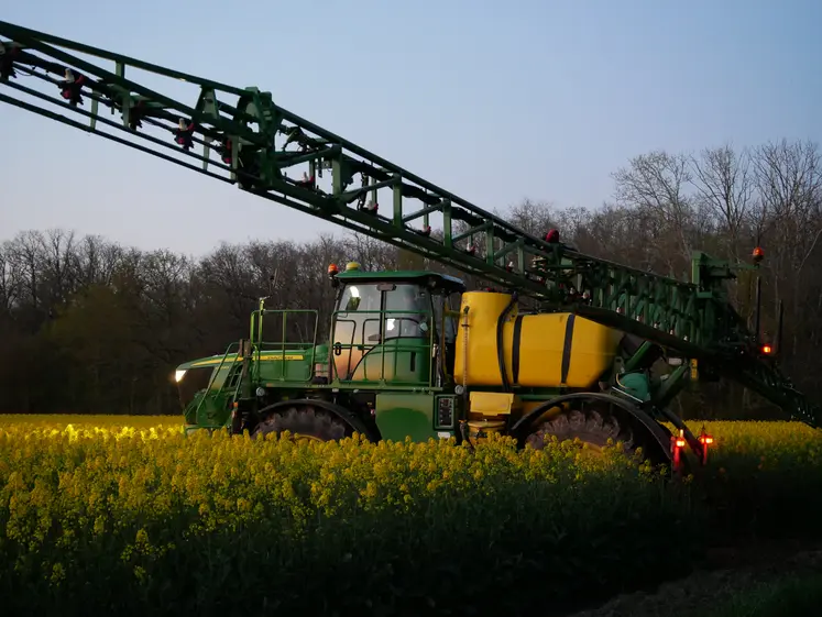 Pulvérisateur effectuant des traitements phytosanitaires le soir dans un champ de colza.