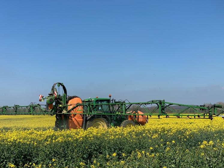 Pulvérisateur dans un champ de colza en fleur sous un ciel bleu.