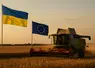 Une moissonneuse batteuse en action pour la moisson 2025 dans un champ de blé avec les drapeaux de l'Ukraine et de l'UE en arrière plan.