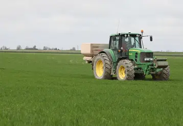 Tracteur qui épand des engrais dans un champ de blé.