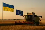 Une moissonneuse batteuse en action pour la moisson 2025 dans un champ de blé avec les drapeaux de l'Ukraine et de l'UE en arrière plan.