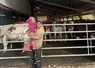 Un éleveur avec sa petite fille dans ses bras devant ses vaches rentrées dans la stabulation.