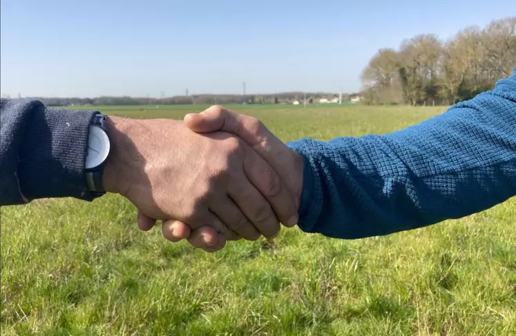 Deux personnes se serrent la main dans un champ.