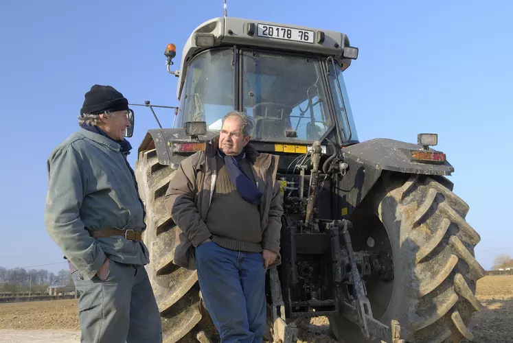 Deux agriculteurs aux cheveux gris discutant devant un tracteurs