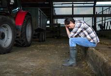 Dans un hangar près de son tracteur, un agriculteur assis se tient la tête dans les mains