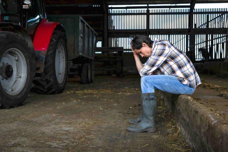 Dans un hangar près de son tracteur, un agriculteur assis se tient la tête dans les mains