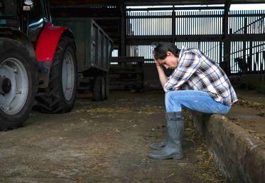 Dans un hangar près de son tracteur, un agriculteur assis se tient la tête dans les mains