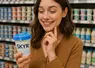 une consommarice au rayon produits laitiers d'un supermarché, hésite en achetant un pot de skyr, elle a l'air joyeuse