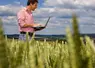 Un agriculteur sur son ordinateur portable dans un champo de blé.