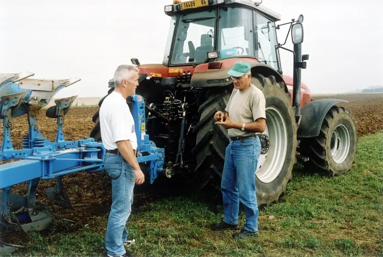 Discussion entre deux membres d'une Cuma devant une machine agricole. 