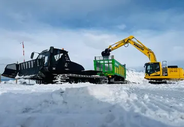 Chantier de transport de neige avec une dameuse tractant une remorque Joskin à chenilles à coté d'une pelle sur chenilles