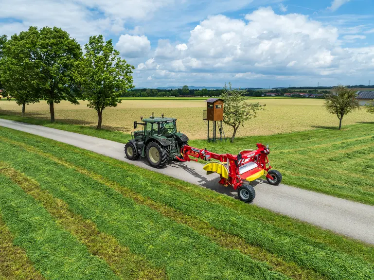 Faucheuse Pottinger NOVACAT T 3100 S RC et tracteur John Deere 6R150 sur la route.