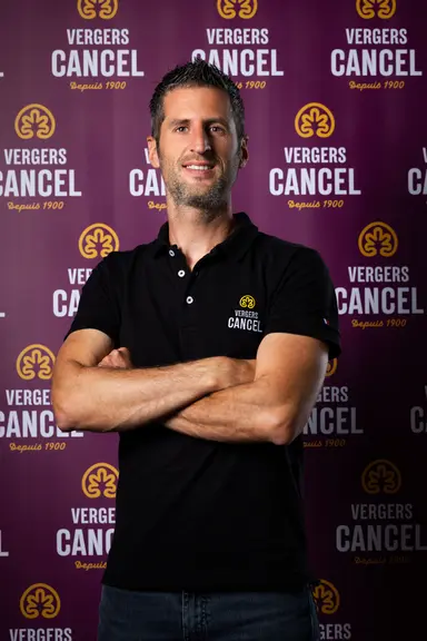 <em class="placeholder">Maxime Gil, directeur général de l’entreprise Vergers Cancel, pose devant un fond avec les logos Vergers Cancel. </em>