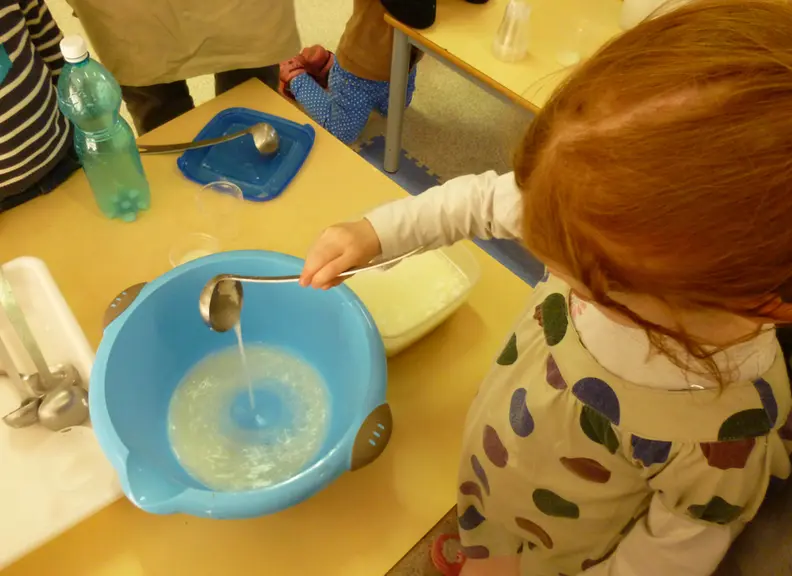 Enfant fabricant du fromage de chèvre, versant du lait avec une louche.