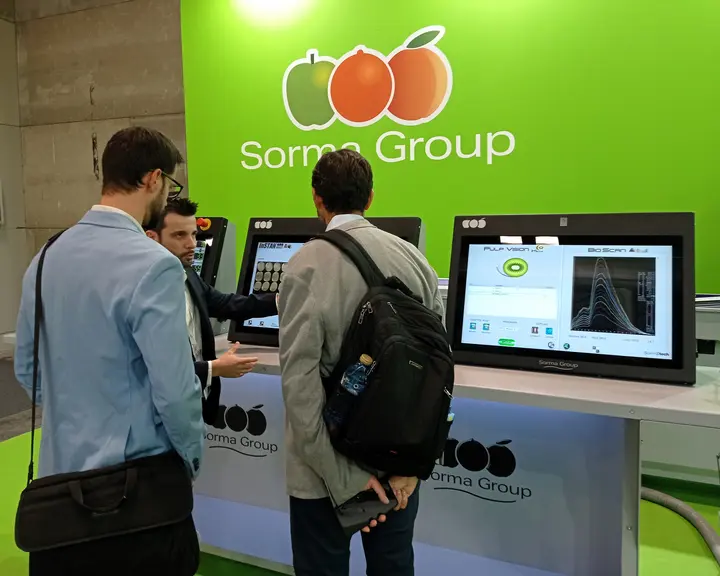 Une personne présente à deux autres personnes comment fonctionne un logiciel de détection des défauts des fruits.