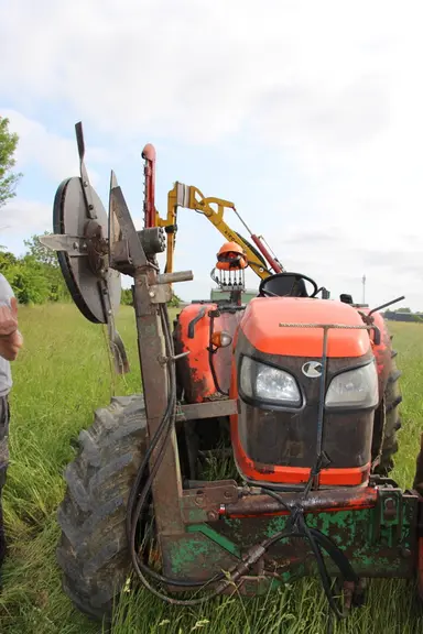 Tracteur équipé d'un bras avec un outil pour couper l'herbe sous les clôtures.