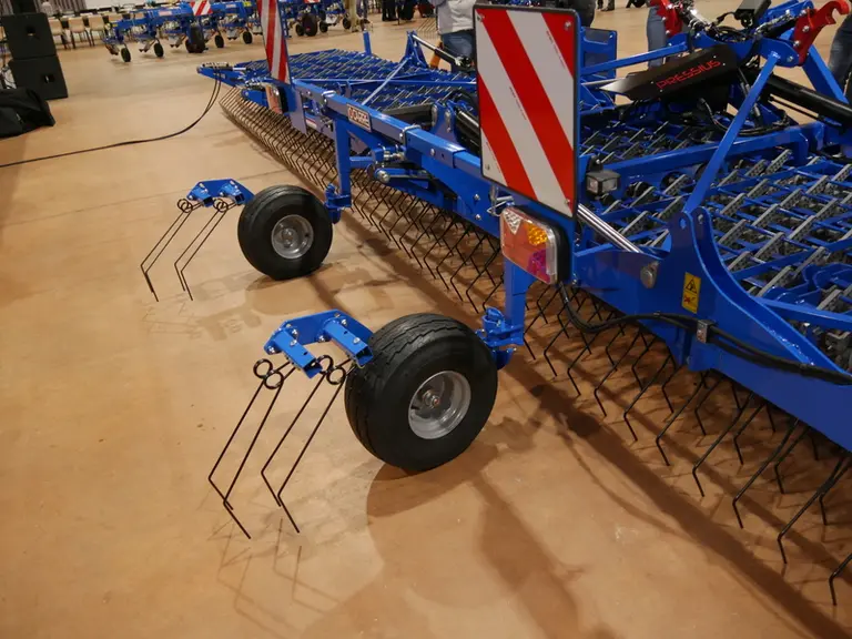 La herse étrille Pressius de Carré de 12,20 mètres de large reçoit à l'arrière deux roues pivotantes participant au bon suivi du sol..