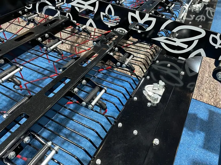 Les dents de la herse étrille Lemken sont chacune reliées par une tringle en acier à des modules hydrauliques intégrés dans la poutre avant du châssis
