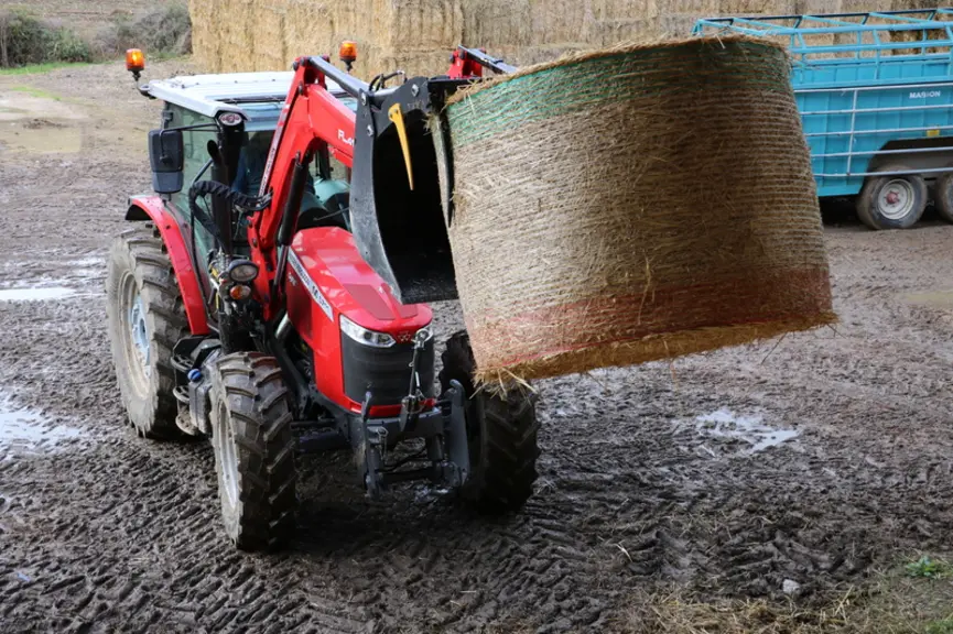 Tracteur Massey Ferguson avec chargeur frontal manipulant une balle ronde.