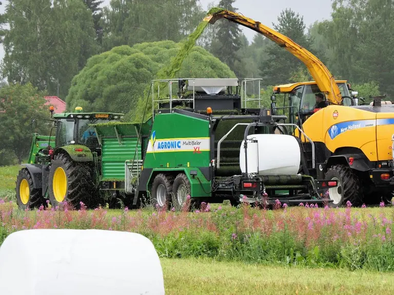 Presse enrubanneuse Knoll Multibaler XLderrière tracteur John Deere et alimentée par ensileuse New Holland FR9060