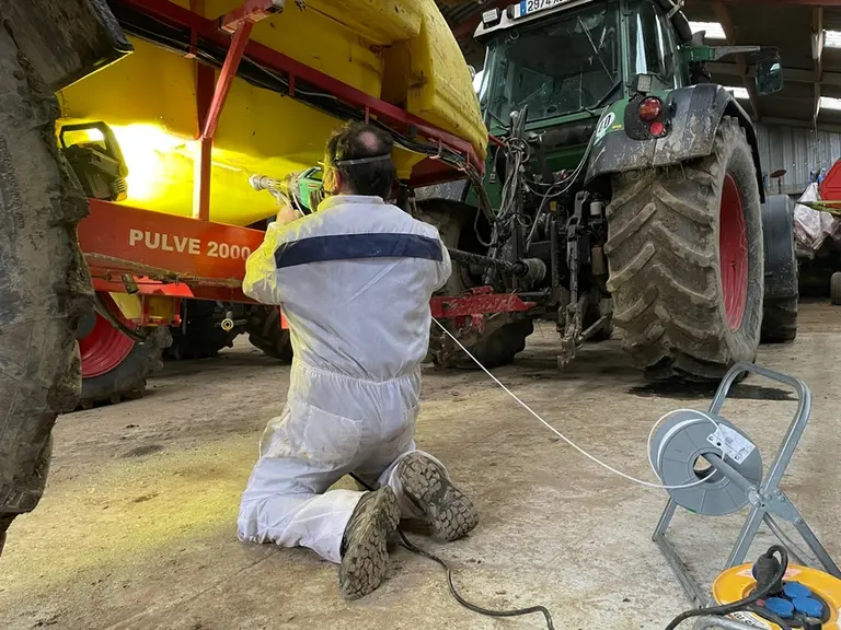 Homme réparant une fuite sur un cuve de pulvérisateur en polyéthylène avec une extrudeuse.