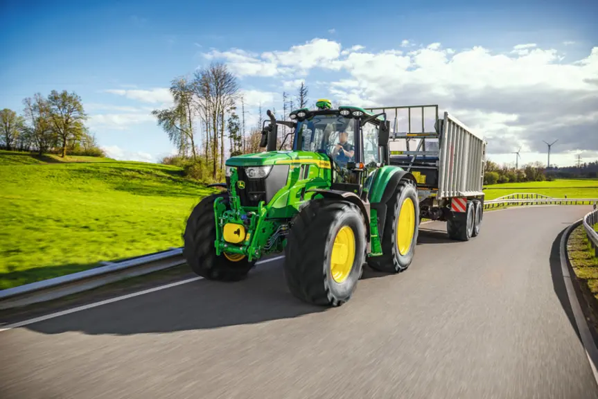 Tracteur John Deere 6M 185 avec une remorque sur la route