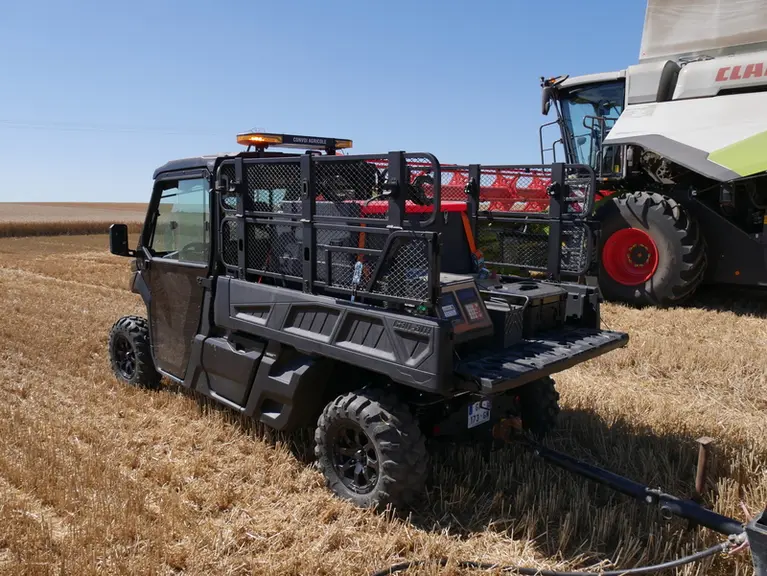 SSV Can-Am avec rehausses de benne grillagées, devant une moissonneuse-batteuse Claas Lexion
