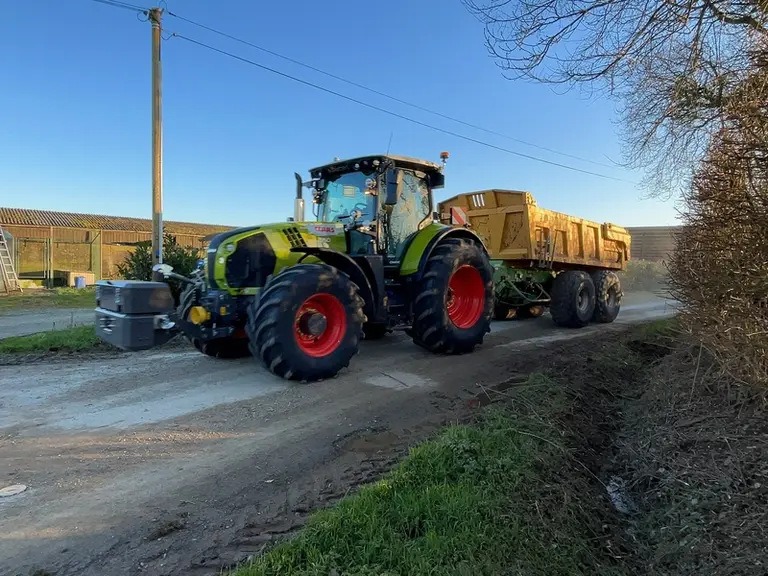 Tracteur Claas Arion 660 CMatic sur la route avec une benne à deux essieux Joskin.
