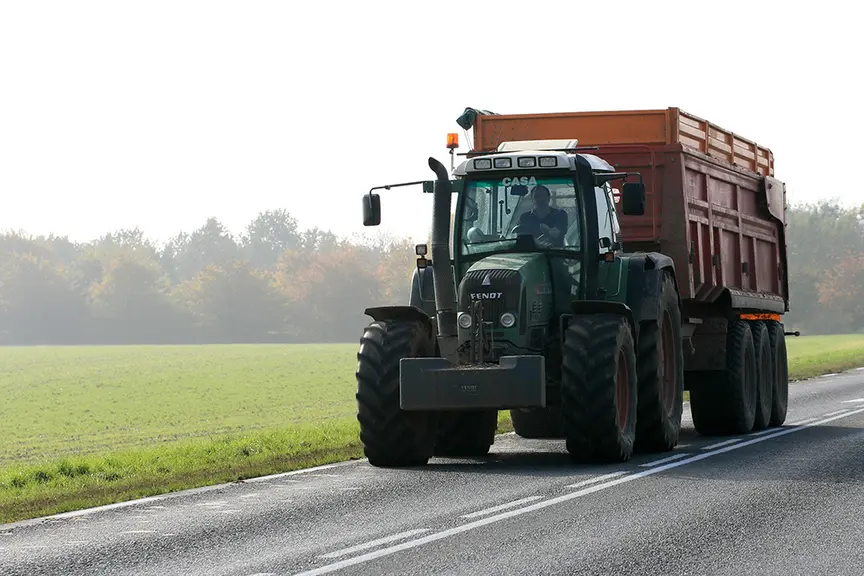 Un tracteur avec remorque roulant sur la route dans la campagne.