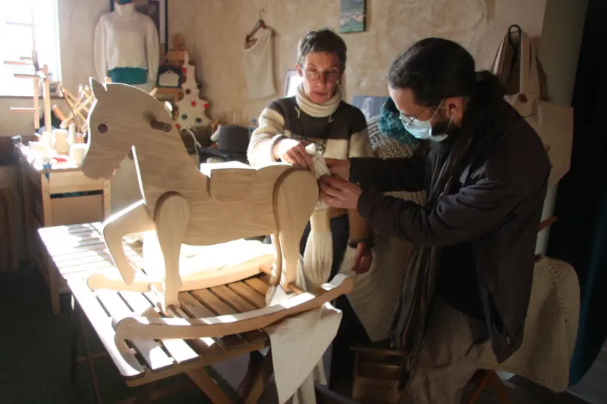 Pour parer ce cheval à bascule d'une crinière et une queue en laine locale, Frédérique et son client Thierry testent différentes possibilités.