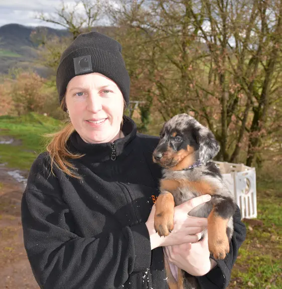 L'éleveuse tient un chiot beauceron dans ses bras en extérieur.