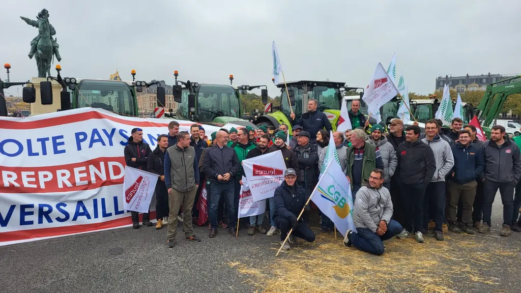 Des agriculteurs sur une botte de paille avec banderole "la révolte paysanne reprend à Versailles" devant le château de Versailles.