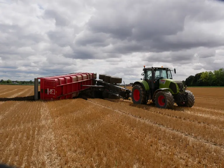 Accident de benne lors de la vidange, benne renversée sur un terrain agricole à côté d'un tracteur.