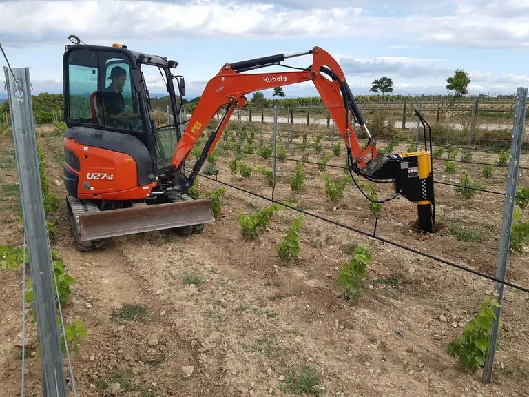 Mini-pelle Kubota dans les vignes équipée d'une complanteuse.