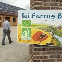 Agriculteur marchant dans sa cour de ferme avec au premier plan une pancarte indiquant "Ici ferme bio"