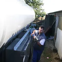 collecte du lait de chèvre : le chauffeur tire un tuyau près de son camion.