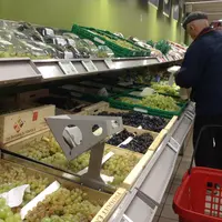 Une personne âgée devant un rayon de raisin dans un supermarché.