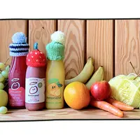 Bouteilles de jus de fruits à marque innocent coiffées de petits bonnets en laine, entourées de divers fruits et légumes