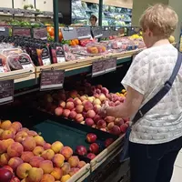 Un rayon de fruits d'été dans un supermarché. Une cliente choisit des pêches.