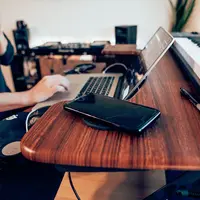 Un Millennial boit une boisson à la paille dans un gobelet jetable tout en travaillant sur son ordinateur portable, son smartphone posé à côté.